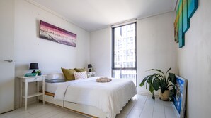 Un dormitorio con cama, mesitas de noche, una ventana y un cuadro en la pared.