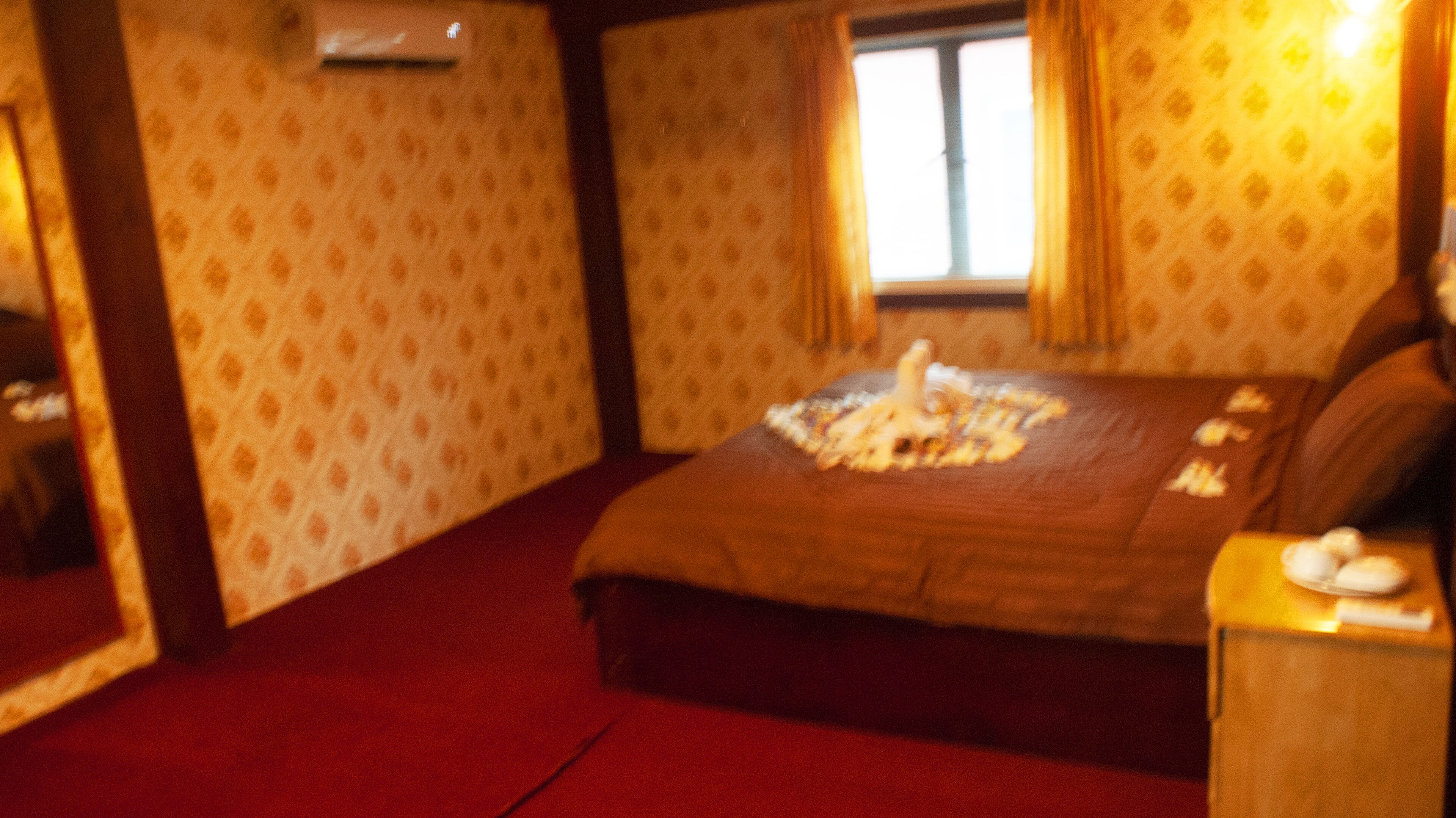 Een slaapkamer met een groot bed, een houten nachtkastje, een spiegel en een raam met gordijnen.