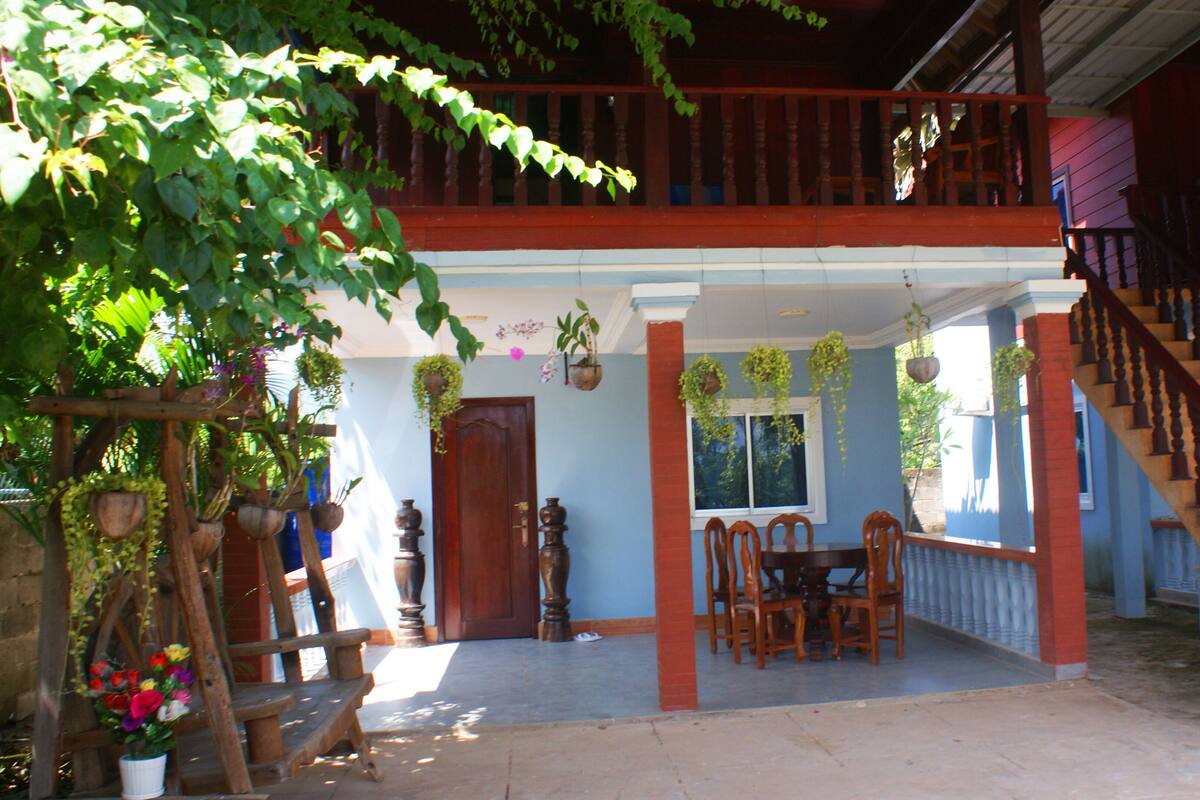 A two-story building with a balcony, a staircase, and a dining area with chairs and a table.