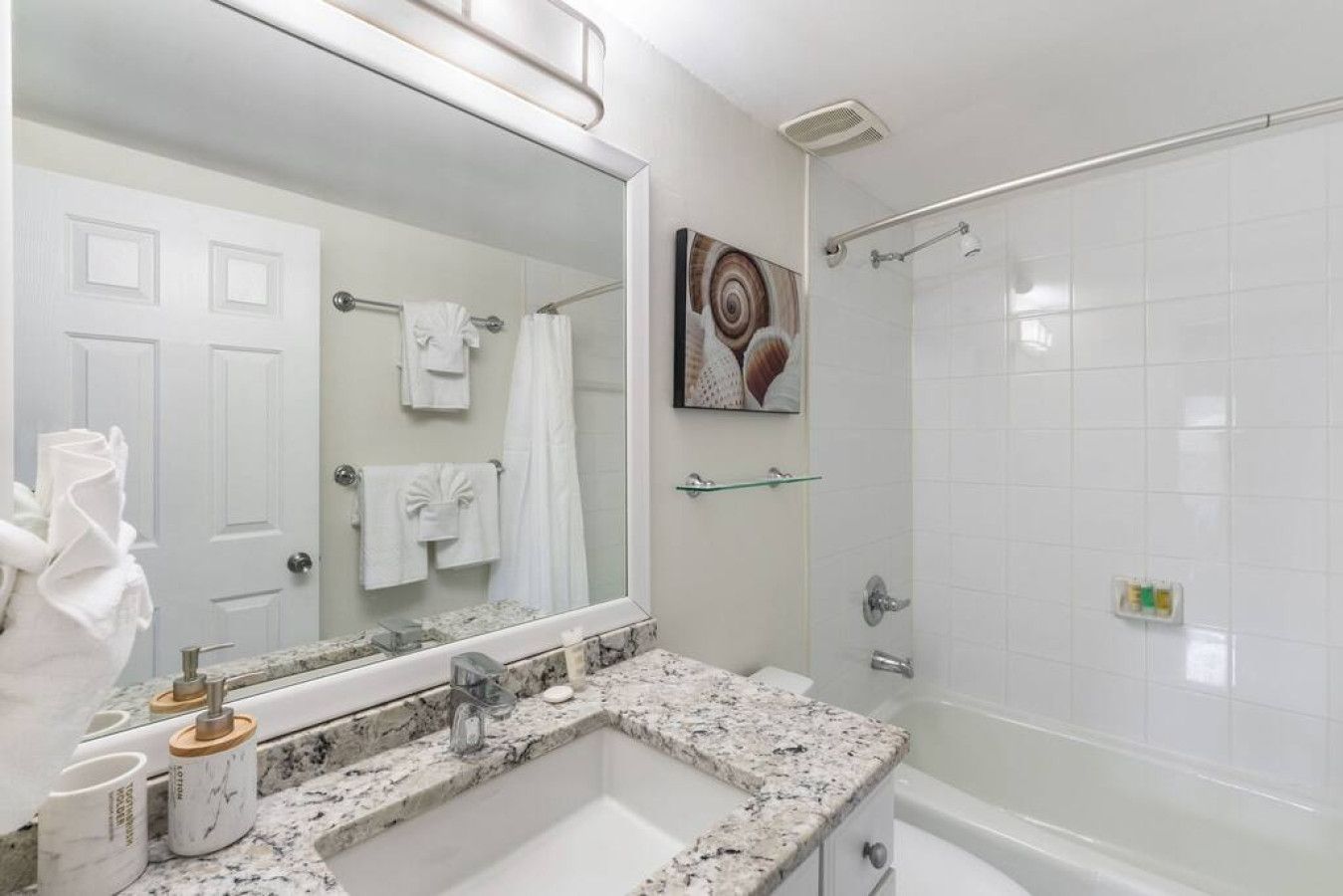 A bathroom with a marble sink, a large mirror, a shower with a glass door, and a towel rack with white towels.