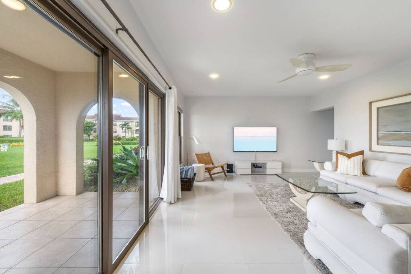 A modern living room with a glass coffee table, white sofas, and a flat-screen TV.