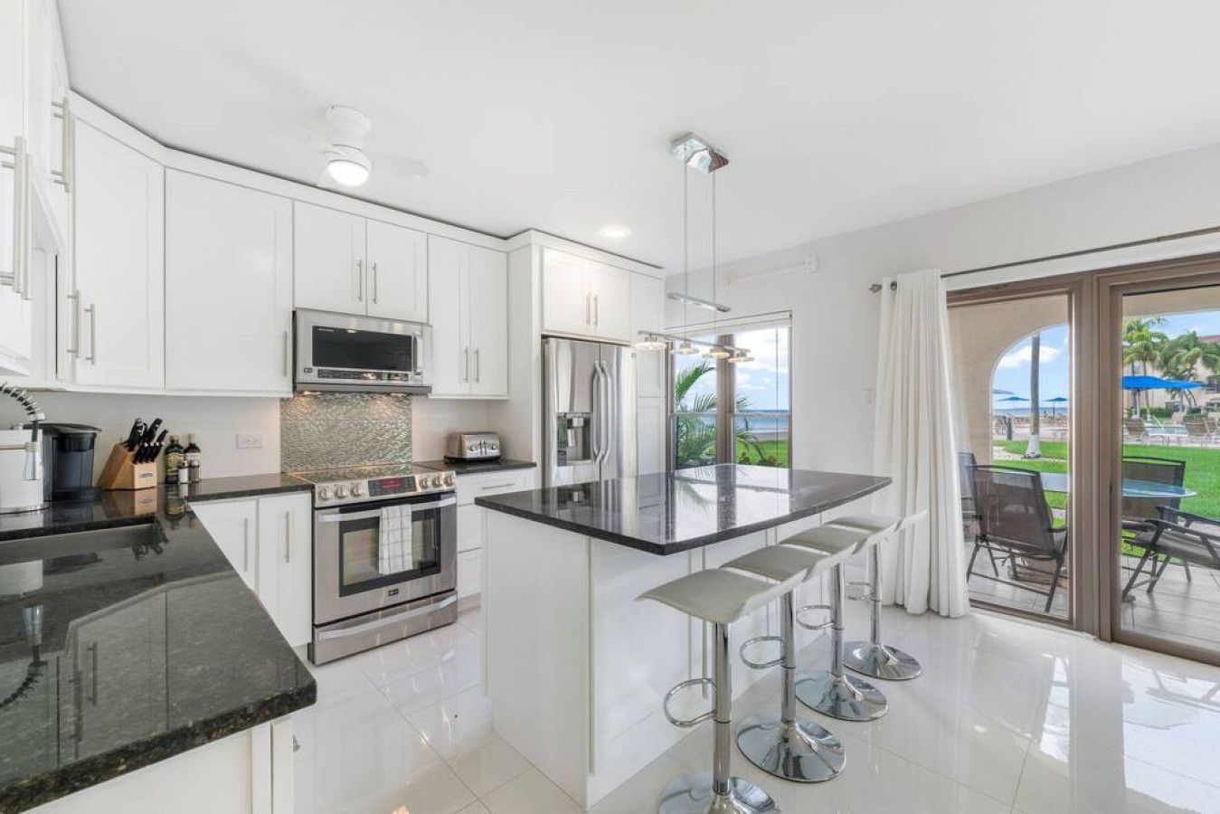 Una cocina moderna con armarios blancos, electrodomésticos de acero inoxidable y una isla grande con taburetes de bar.