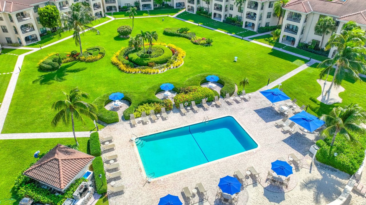 A hotel with a central swimming pool, lounge chairs, and palm trees.