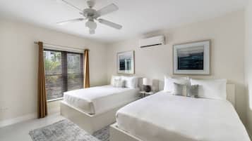 Habitación de hotel con dos camas, ventilador de techo, unidad de aire acondicionado y ventana con persianas.