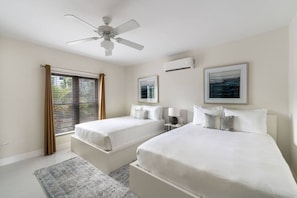 Habitación de hotel con dos camas, ventilador de techo, unidad de aire acondicionado y ventana con persianas.