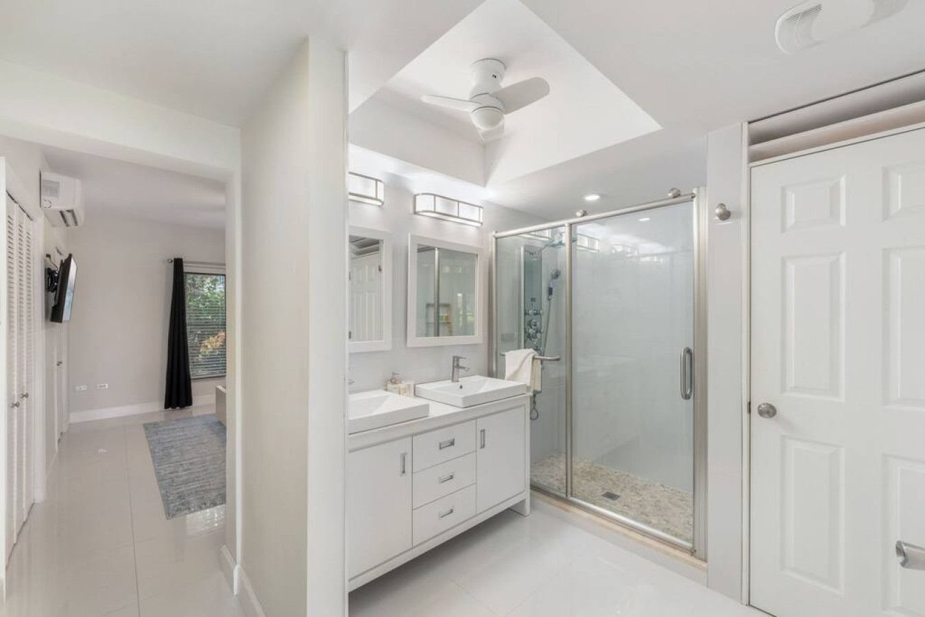 A modern bathroom with a walk-in shower, a ceiling fan, and a large mirror.