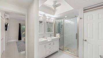 A modern bathroom with a walk-in shower, a ceiling fan, and a large mirror.
