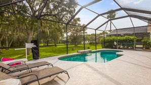 Une piscine extérieure dotée d’un espace abrité, entourée d’arbres et bordée d’une pelouse.