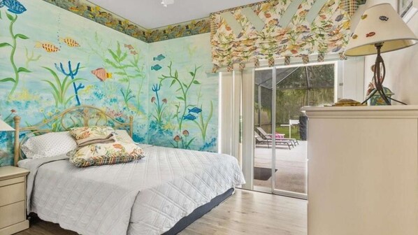 A bedroom with a bed, a nightstand, a dresser, and a window with a view of an outdoor patio. - South facing pool home, gated community, 10 mins to Walt Disney World Resort! (Kissimmee)