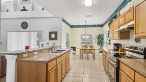 Une cuisine moderne avec des meubles en bois, un grand îlot central, un coin repas avec une table et des chaises, et une vue sur le salon.