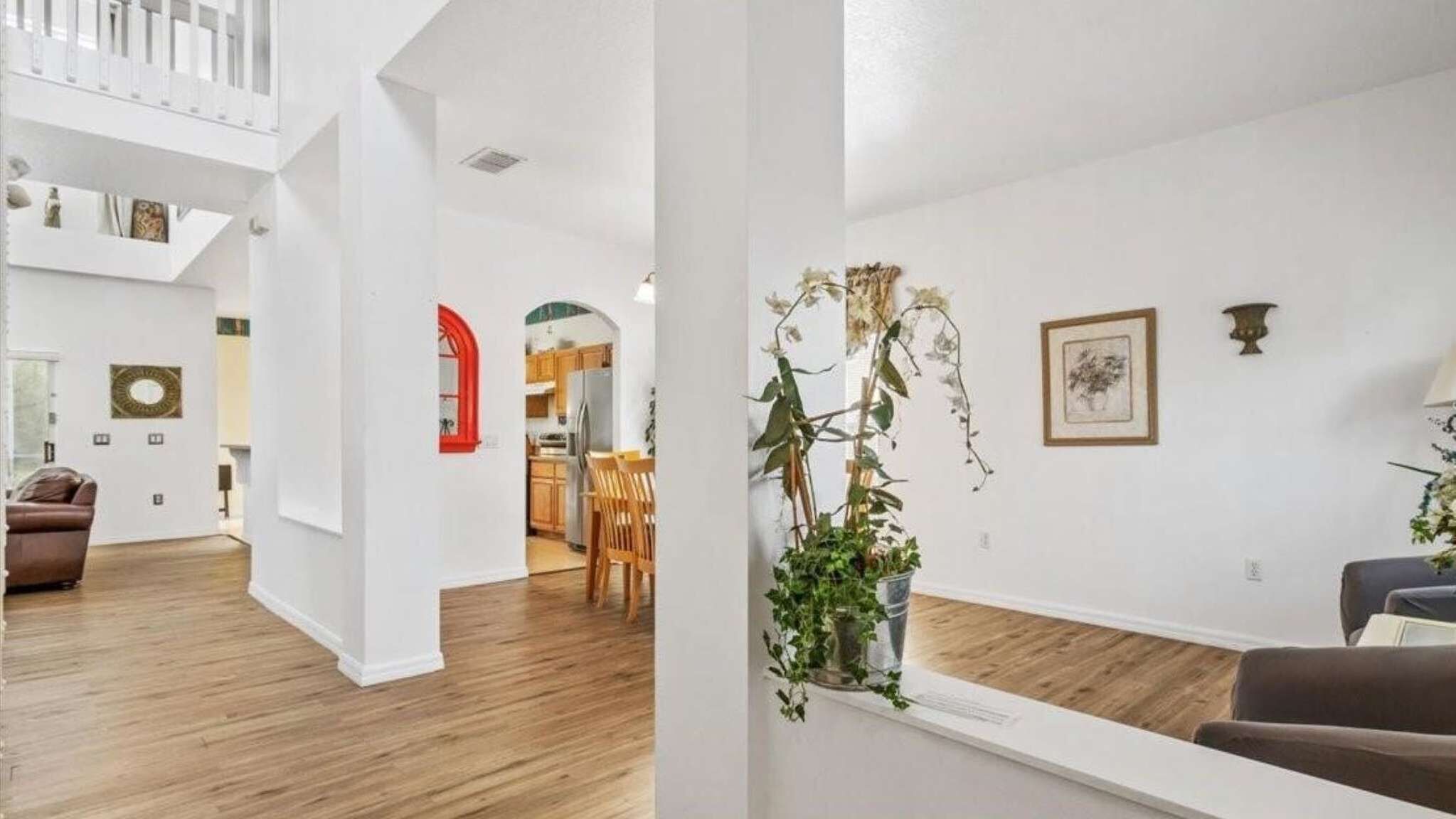 Un'ampia zona giorno con soffitto alto, pavimento in legno e composizione floreale al centro.