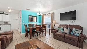 A living room with a brown leather couch, a wooden coffee table, and a dining area with a turquoise wall and wooden chairs. - LJ's Cottages 4 BALCONY BEACH AND POOL (Sarasota)