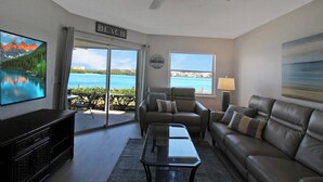 A living room with a view of a lake, a ceiling fan, a television, and a sign that reads "BEACH".