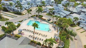 A residential area with a swimming pool surrounded by lounge chairs and umbrellas, with houses in the background.