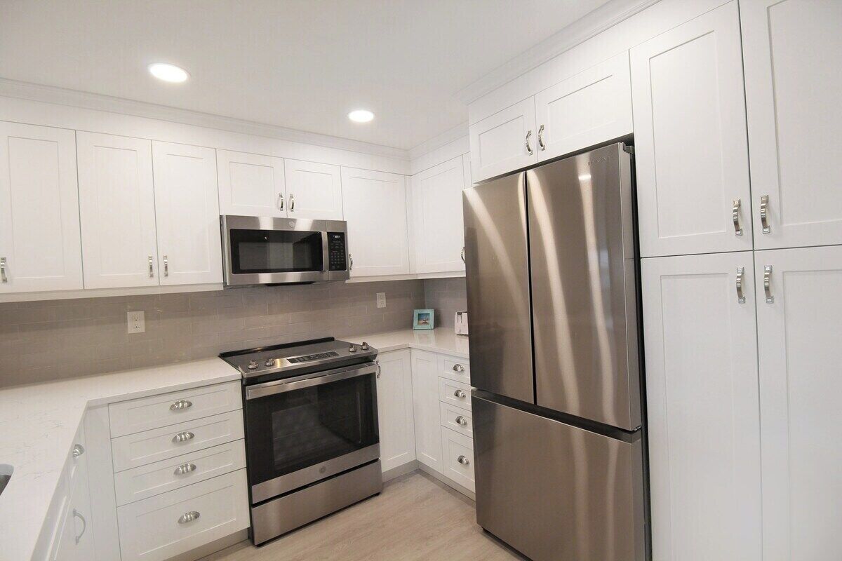 A modern kitchen with white cabinetry, stainless steel appliances, and a built-in oven.