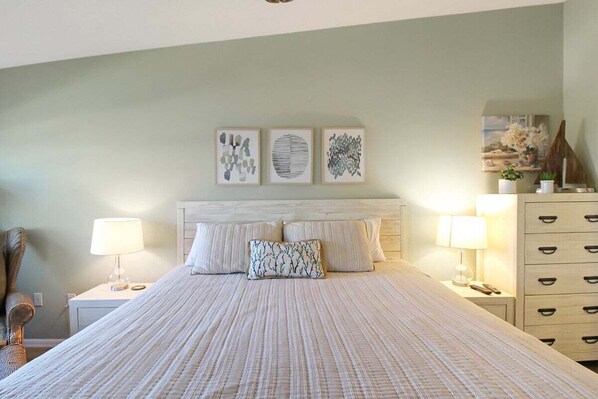 A neatly arranged bedroom with a large bed, two bedside tables with lamps, a chair, and wall art. - 2nd floor bayfront Siesta Key condo with beach access - GBB 1373 (Sarasota)