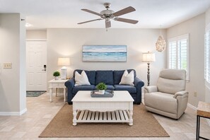 A living room with a blue sofa, a white coffee table, a beige armchair, a ceiling fan, and a painting on the wall. - Charming 2/2 Siesta Key condo with beach access - GBB 1338 (Sarasota)