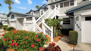 A residential building with a white exterior, a staircase leading to the entrance, and a well-maintained garden with red flowers. - Bayfront Siesta Key condo with amazing views - GBB 1391 (Siesta Key)