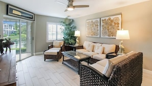 A living room with a sofa, chairs, a coffee table, and a ceiling fan. There is a window with a view of a house and a dog outside. - Lakefront Siesta Key condo with beach access - GBB 1313 (Sarasota)