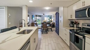 A modern kitchen with a central island, built-in oven, microwave, and a dining area with a table and chairs. - Lakefront Siesta Key condo with beach access - GBB 1313 (Sarasota)