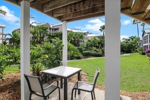 Patio esterno con tavolo e sedie, circondato da vegetazione lussureggiante e vista su edifici residenziali.
