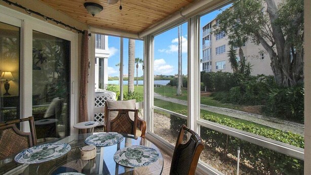 Aurinkoinen huone, jossa on suuret ikkunat, kattotuuletin ja pöytä tuoleineen.