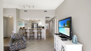 Una cocina moderna con una isla central, taburetes de bar y un televisor de pantalla plana grande sobre un mueble blanco.