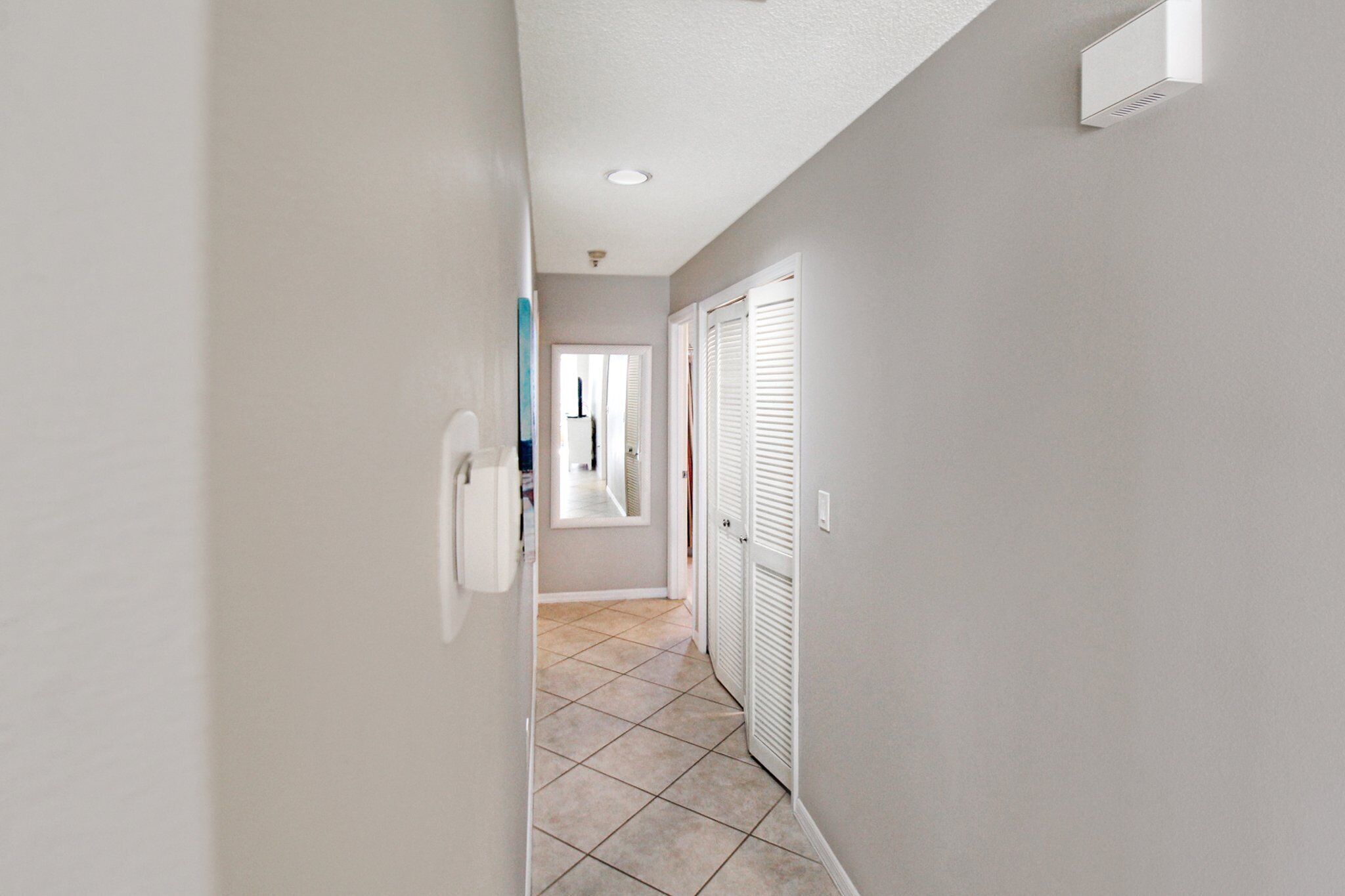 A narrow hallway with a tiled floor, white walls, and a door with white shutters.