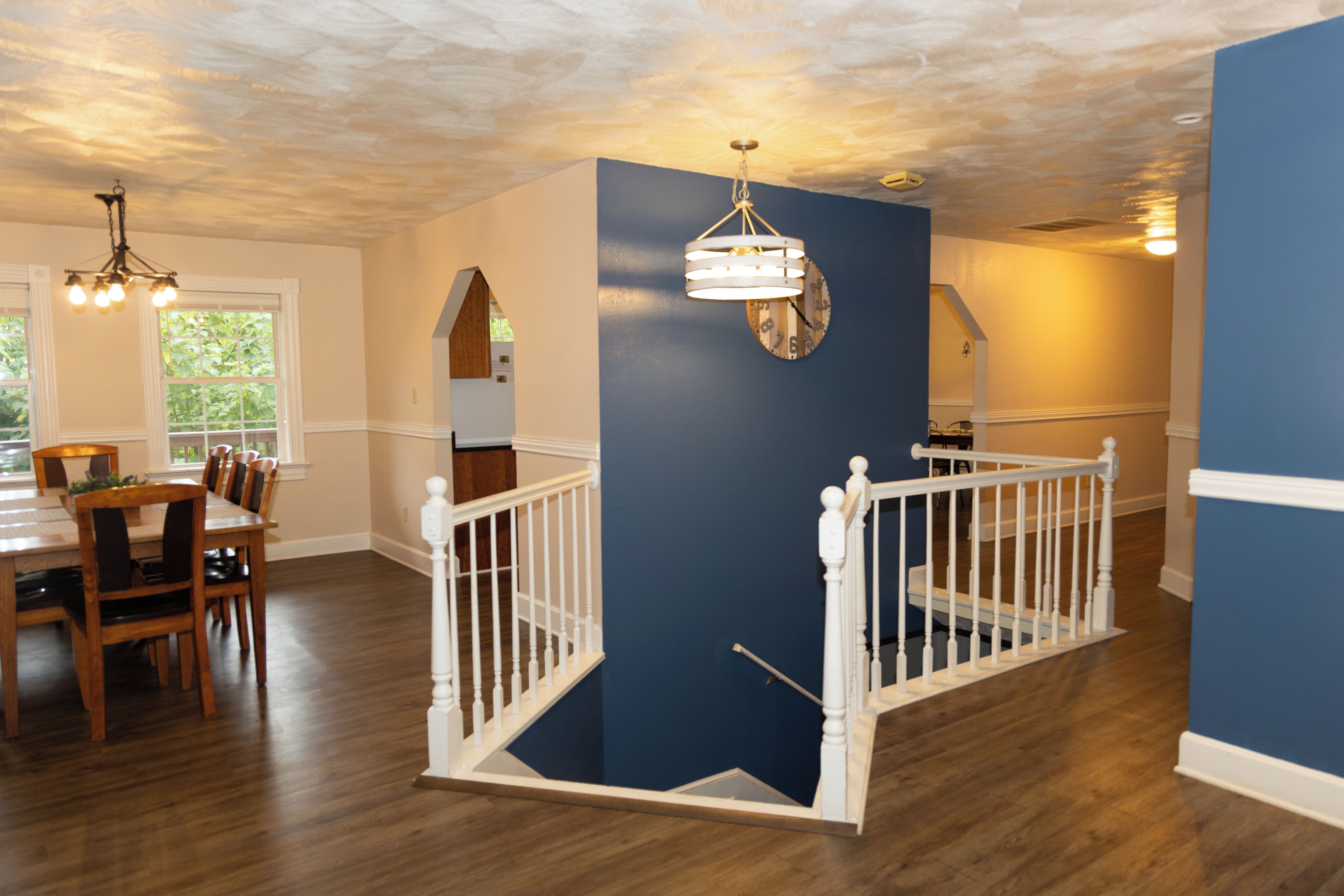 A dining area with a wooden table and chairs, a staircase with white railings, and a blue accent wall.