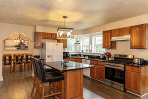 A modern kitchen with wooden cabinets, a central island, stainless steel appliances, and a dining area with chairs. - Sunridge Retreat is a secluded cabin in Luray, VA for large family and friends (Luray)
