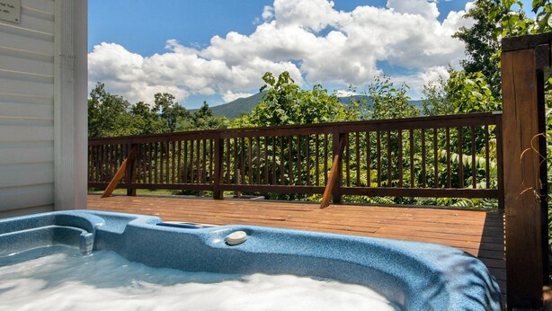 Un bain à remous sur une terrasse en bois, avec vue sur une montagne et des arbres.