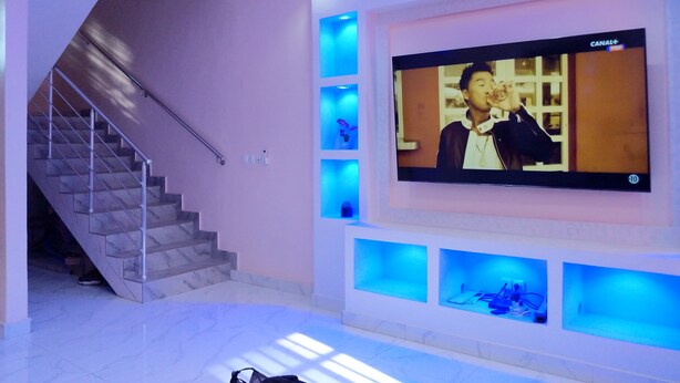 Ein modernes Interieur mit einem großen Flachbildfernseher an der Wand, einer Treppe mit Metallgeländer und Einbauleuchten.