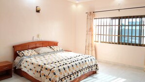 Ein Schlafzimmer mit einem hölzernen Bett, einem Nachttisch, einem Deckenventilator und einem Fenster mit Gitterstäben.