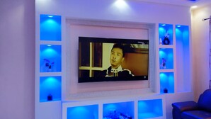 Ein Wohnzimmer mit einem großen Flachbildfernseher, der an einer weißen Wand befestigt ist, umgeben von blauen Regalen und einem schwarzen Ledersofa.