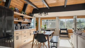 Una cocina moderna con armarios de madera, un refrigerador negro y un comedor con mesa y sillas.