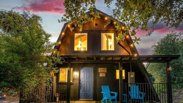 Una cabaña de madera con un porche, dos ventanas y una puerta.