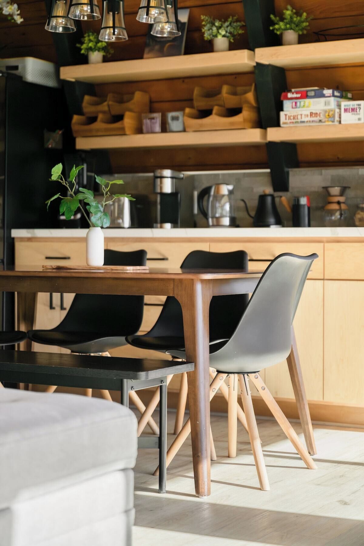 Une cuisine moderne avec des meubles en bois, une table à manger avec des chaises et des luminaires suspendus.