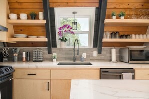 A modern kitchen with wooden shelves, a central window, and a sink.