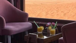 A room with a view of a desert landscape, featuring a bed, two armchairs, and a small table with drinks and a flower. - Wadi Rum Rose camP (Wadi Rum)