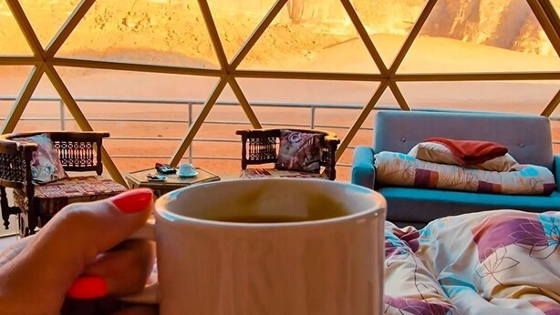 A person holding a mug inside a geodesic dome structure with a desert view. - Wadi Rum Rose camP (Wadi Rum)