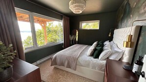 Ein Schlafzimmer mit einem großen Bett, zwei Fenstern, einer Chandelier und Blick auf Bäume.