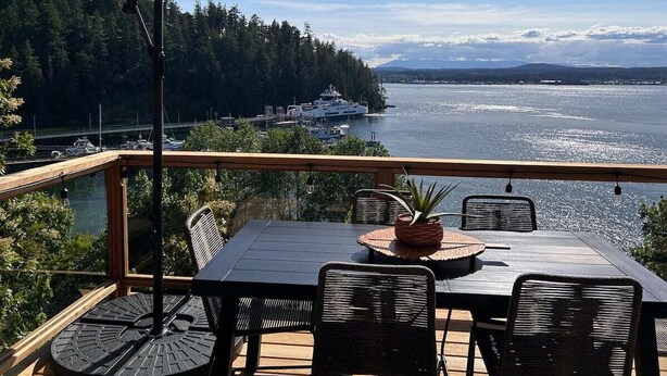 Eine Terrasse mit Tisch und Stühlen, mit Blick auf ein Gewässer mit Booten und einem bewaldeten Ufer im Hintergrund.