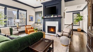 A living room with a fireplace, green sofa, and a TV mounted above it. - Lockeland Luxe｜Walk to 5 Points｜2 mi to Broadway (Nashville)