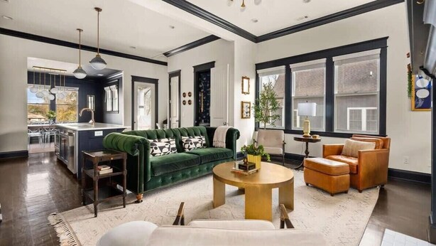 A spacious living room with a green sofa, a round coffee table, and a leather armchair. A kitchen is visible in the background with a large window. - Lockeland Luxe｜Walk to 5 Points｜2 mi to Broadway (Nashville)