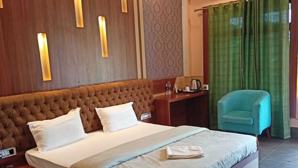 Een hotelkamer met een groot bed, een houten hoofdbord, een nachtkastje, een bureau, een stoel en een groen gordijn.