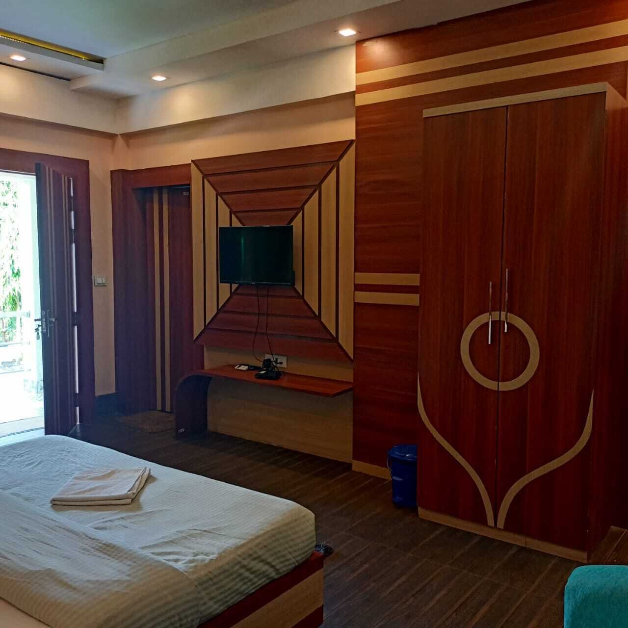A hotel room with a bed, a television mounted on a wooden wall, a wardrobe, and a small table with a chair.