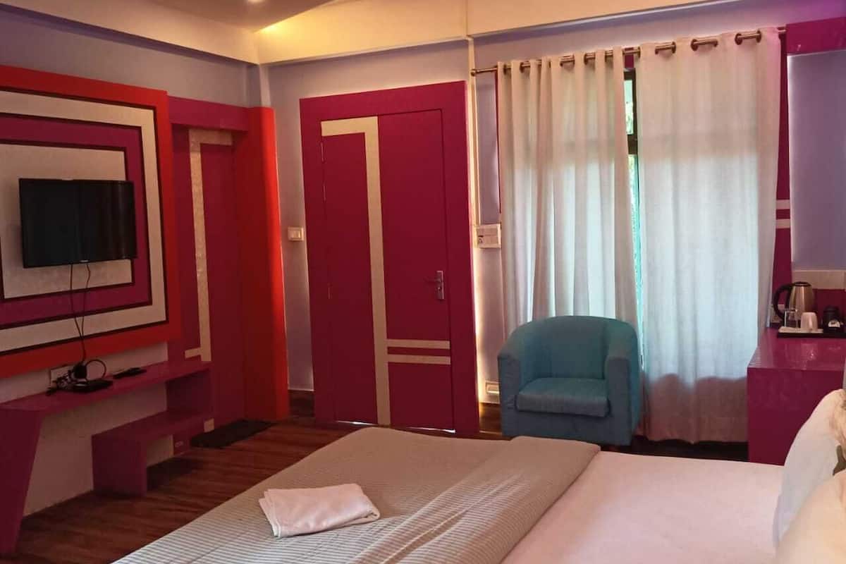 Quarto de hotel com cama, poltrona, televisão na parede e janela com cortinas.