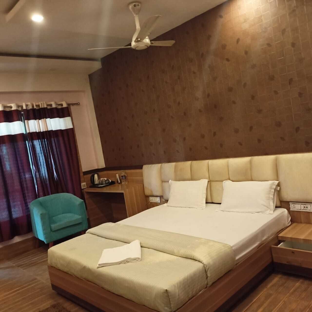 Hotelkamer met een groot bed, een plafondventilator, houten paneelwanden, een groene fauteuil en een houten nachtkastje.
