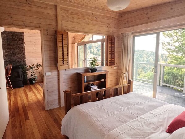 Un dormitorio de cabaña de madera con una cama, chimenea y balcón con vistas al bosque.