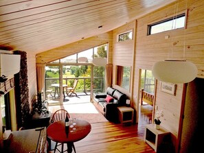 A cozy, wooden interior with a dining area, a sofa, and a view of the outdoors.